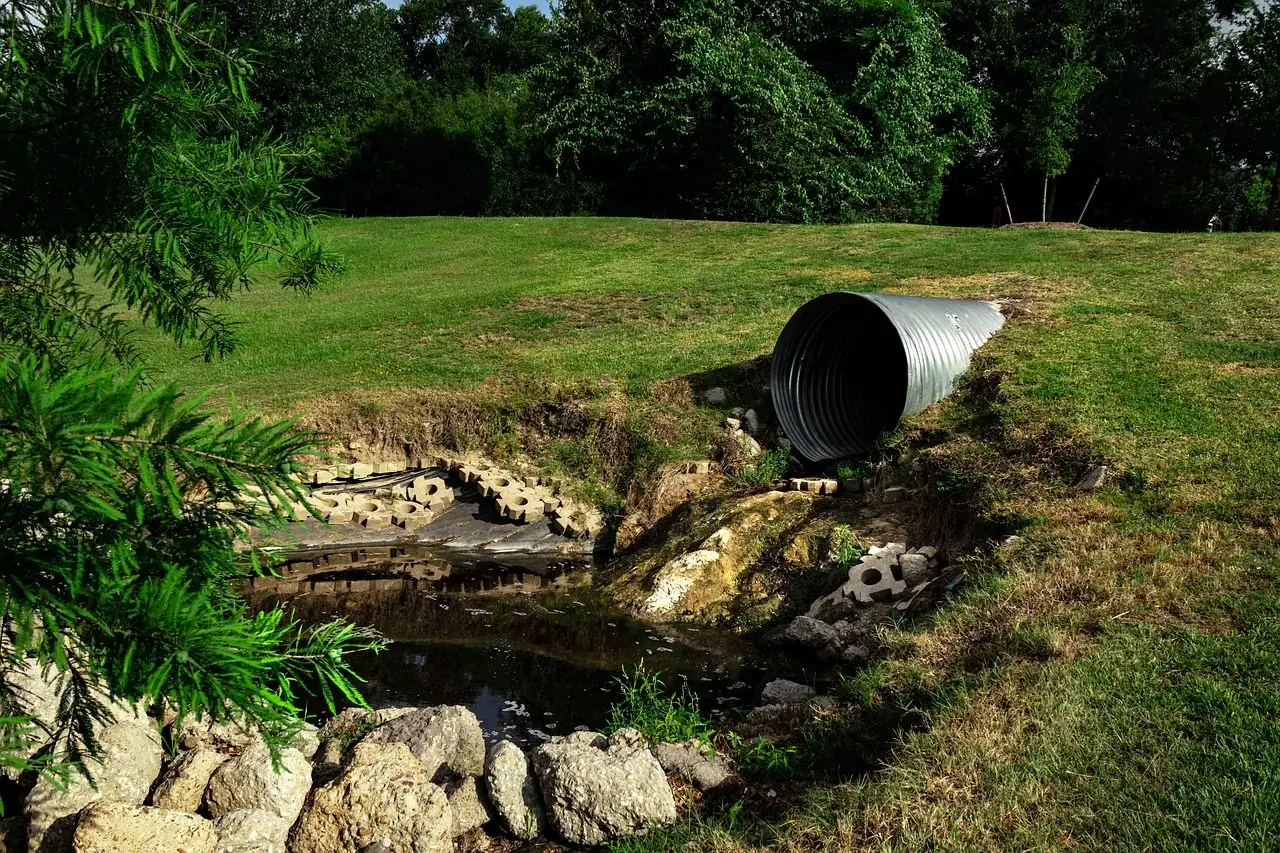 Corrugated metal culvert pipe opening into a small creek among trees
