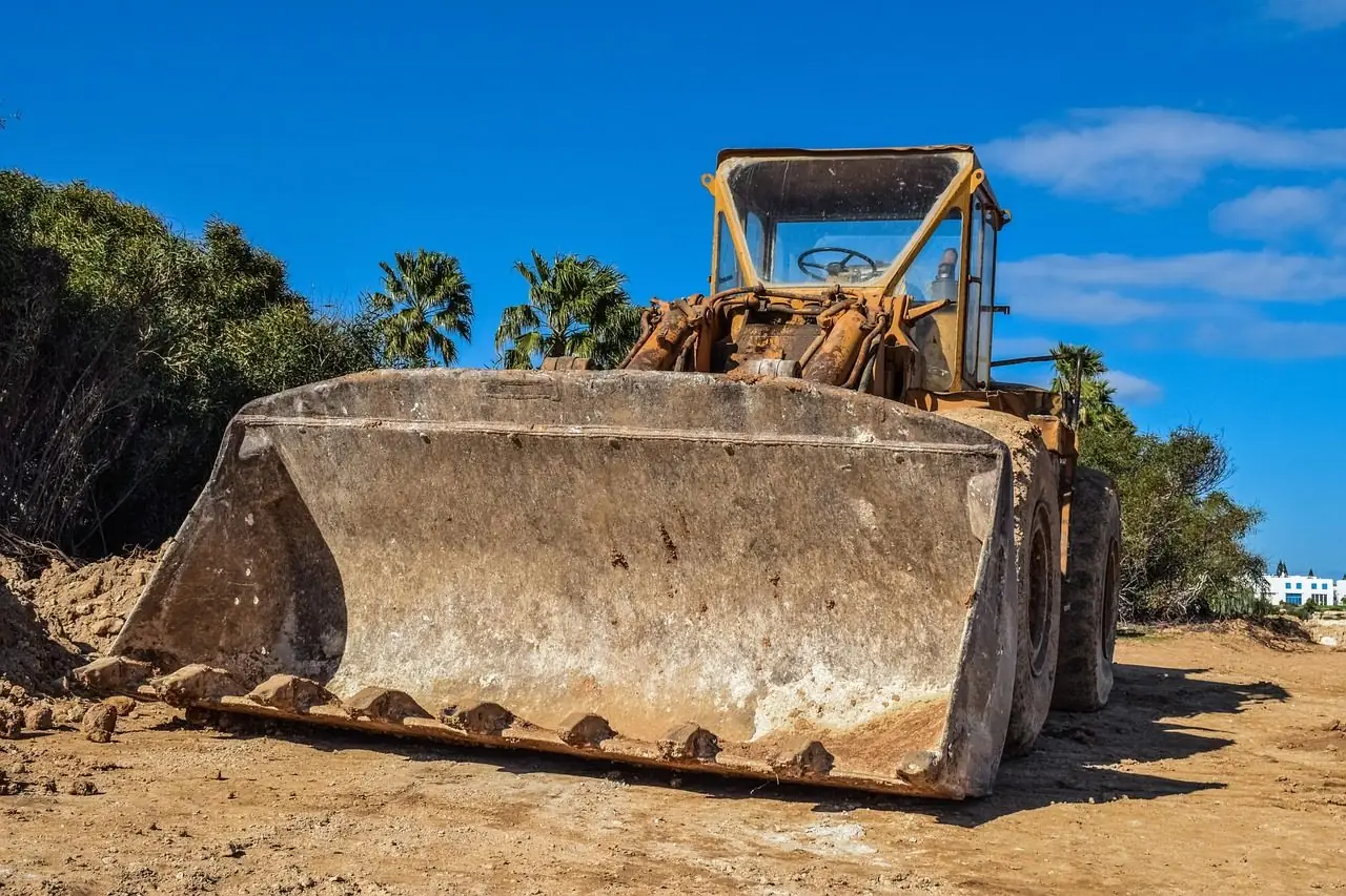 Bulldozer with a raised blade in front of palm trees on a dirt site