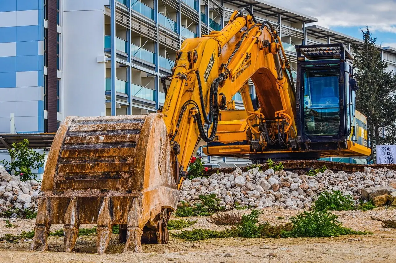 Yellow excavator bucket in the foreground on a city construction site