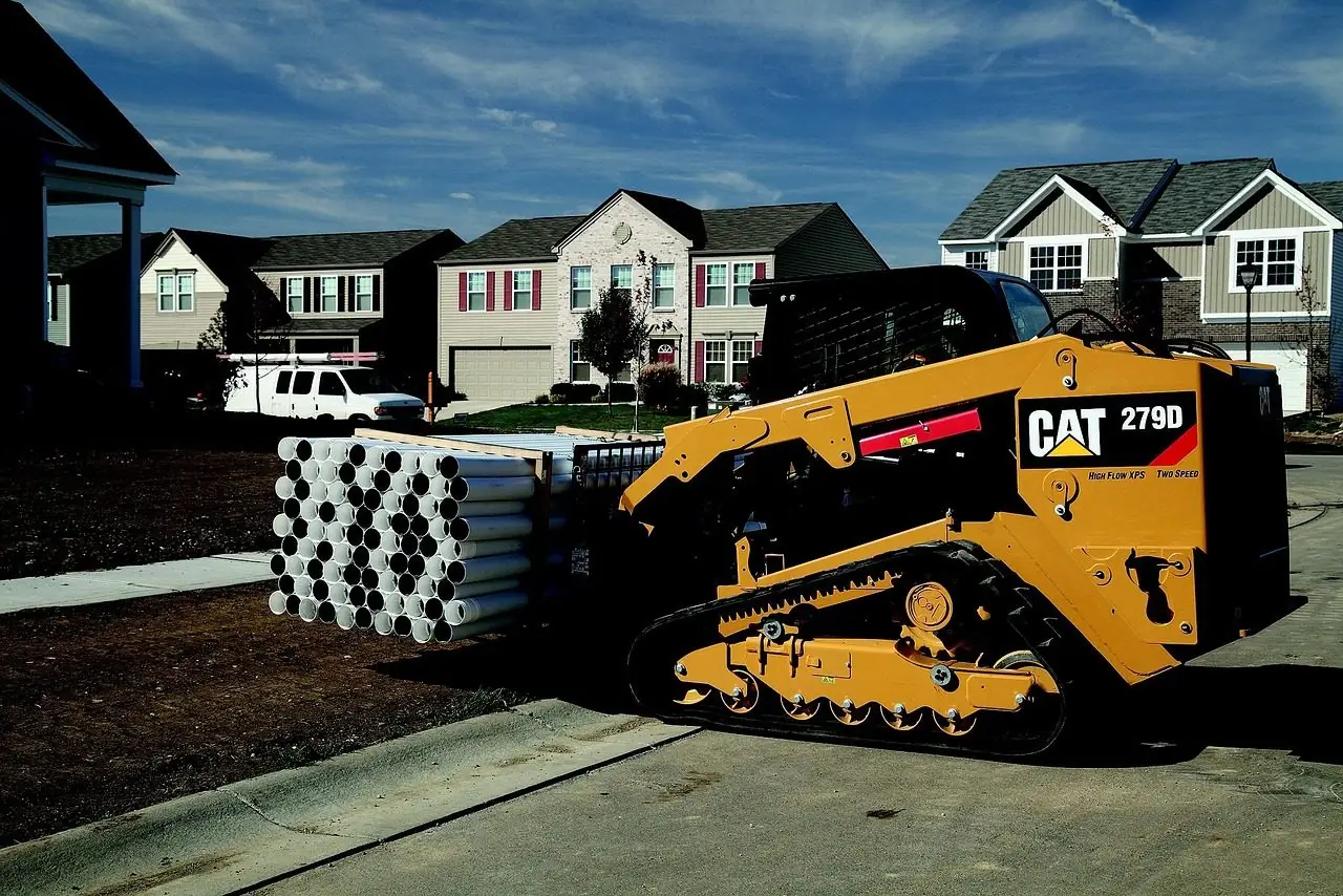 Tracked skid steer loader parked by stacks of pipe in a new subdivision