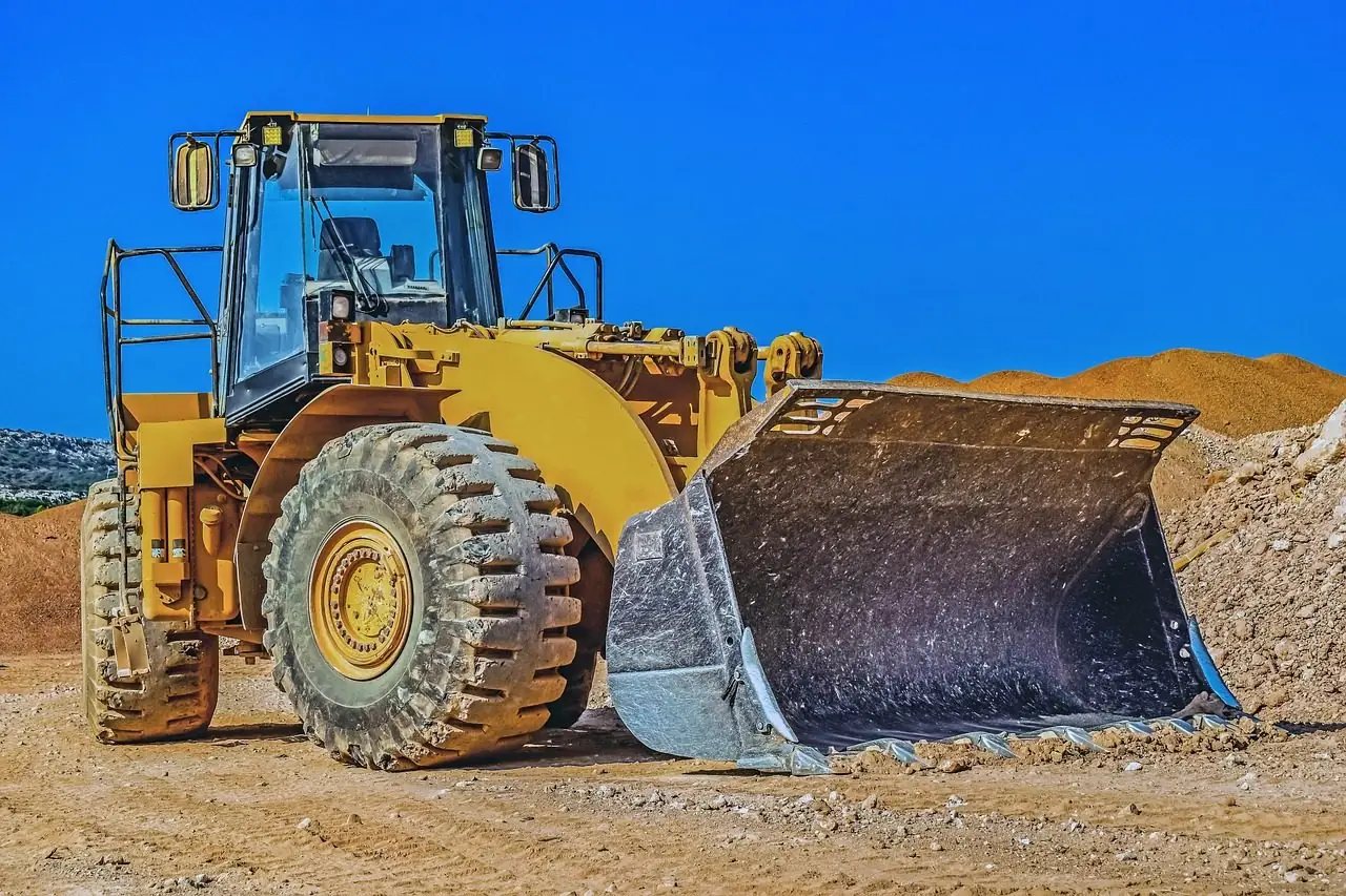 Yellow wheel loader with its bucket lowered in front of a dirt pile